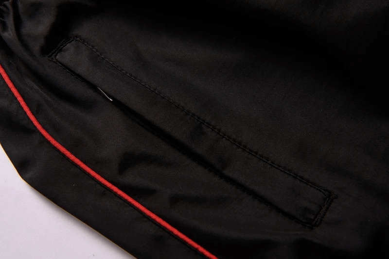 Close-up of black tracksuit pants with red piping and pocket detail, showcasing stylish men's sportswear design.